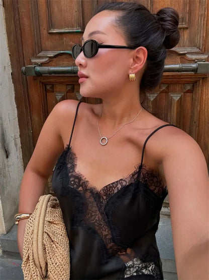 Woman wearing a black lace top with gold jewelry in front of a wooden door.